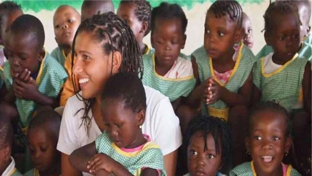 Una volontaria sorride circondata da bambini in divisa scolastica in un'aula di Inhassoro