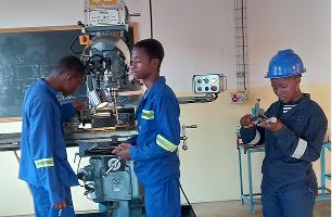 Tre studenti con tuta e casco al lavoro su un trapano nel laboratorio di meccanica