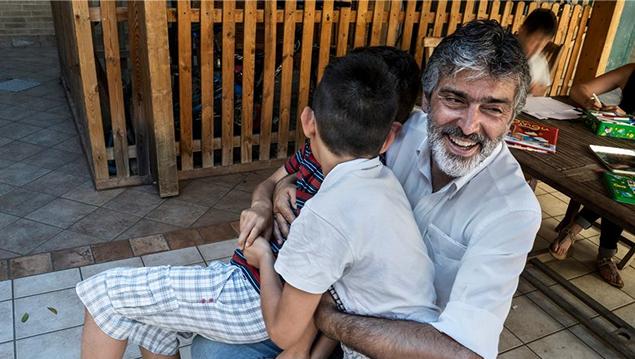 Ugo Bressanello abbraccia sorridente due bambini in uno spazio all'aperto di Domus de Luna