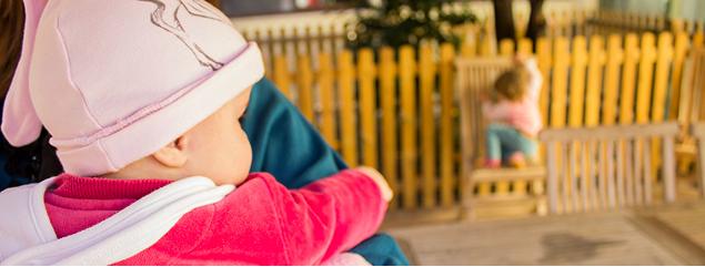 Un'educatrice tiene in braccio una bambina in uno spazio all'aperto di Domus de Luna, mentre altri bambini giocano sullo sfondo