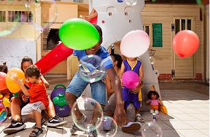 Bambini ed educatrici giocano con palloncini e bolle di sapone nel cortile di una comunità di Domus de Luna